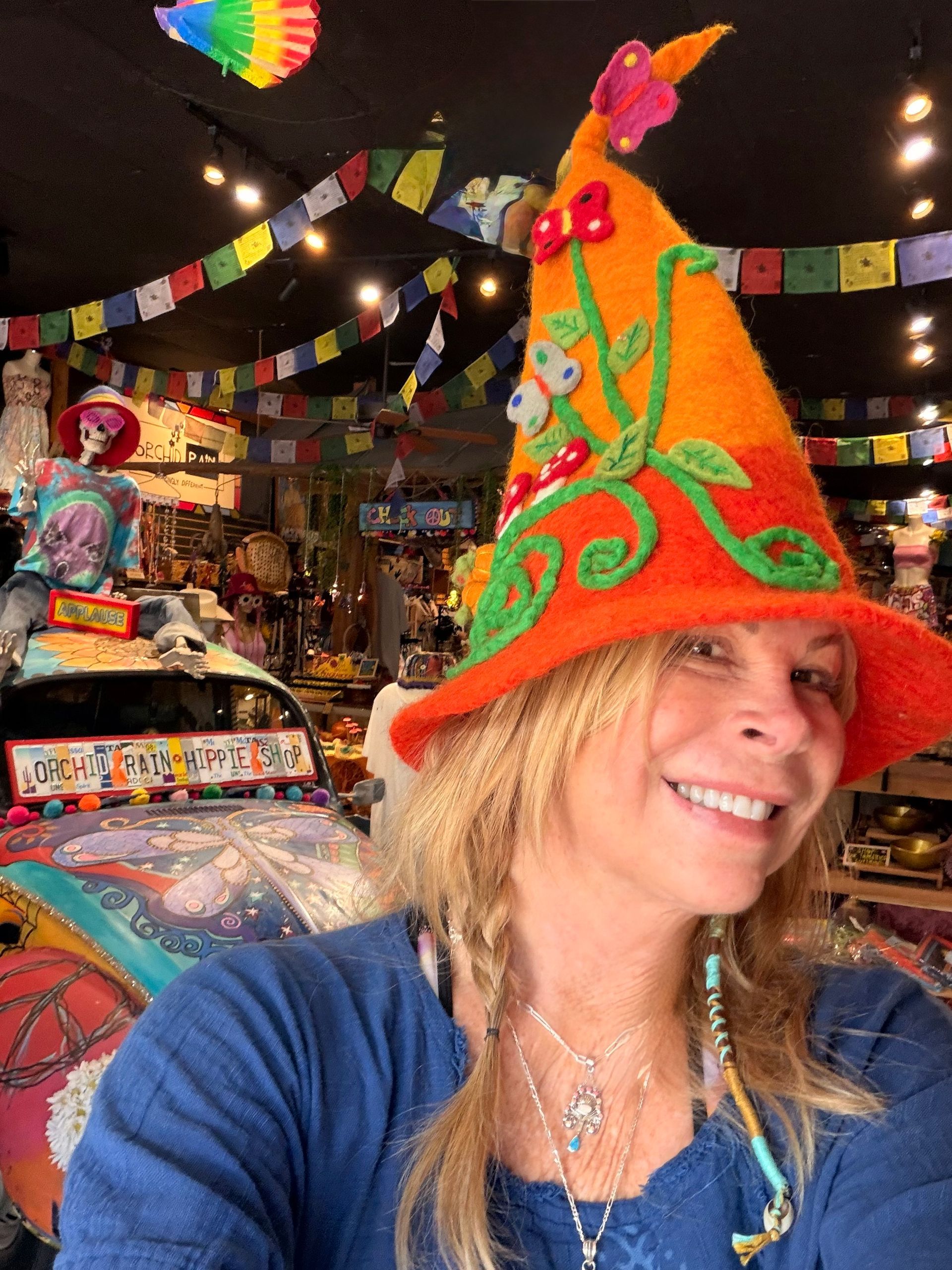 Smiling woman in a colorful pointed hat, standing in a festively decorated room with hanging banners and bright patterns