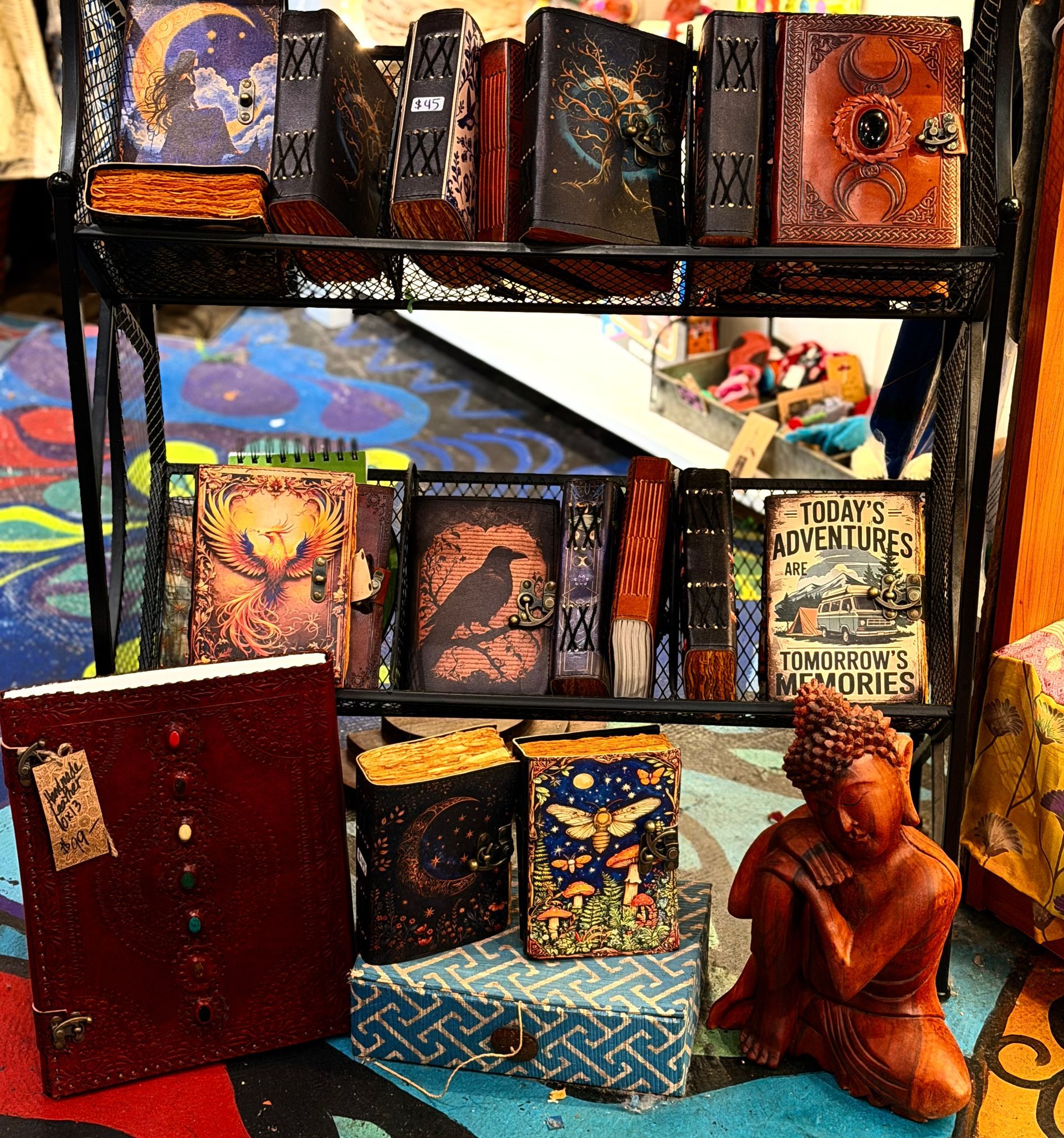 Colorful display of handmade books and artwork on shelves, with a small seated figurine in the foreground