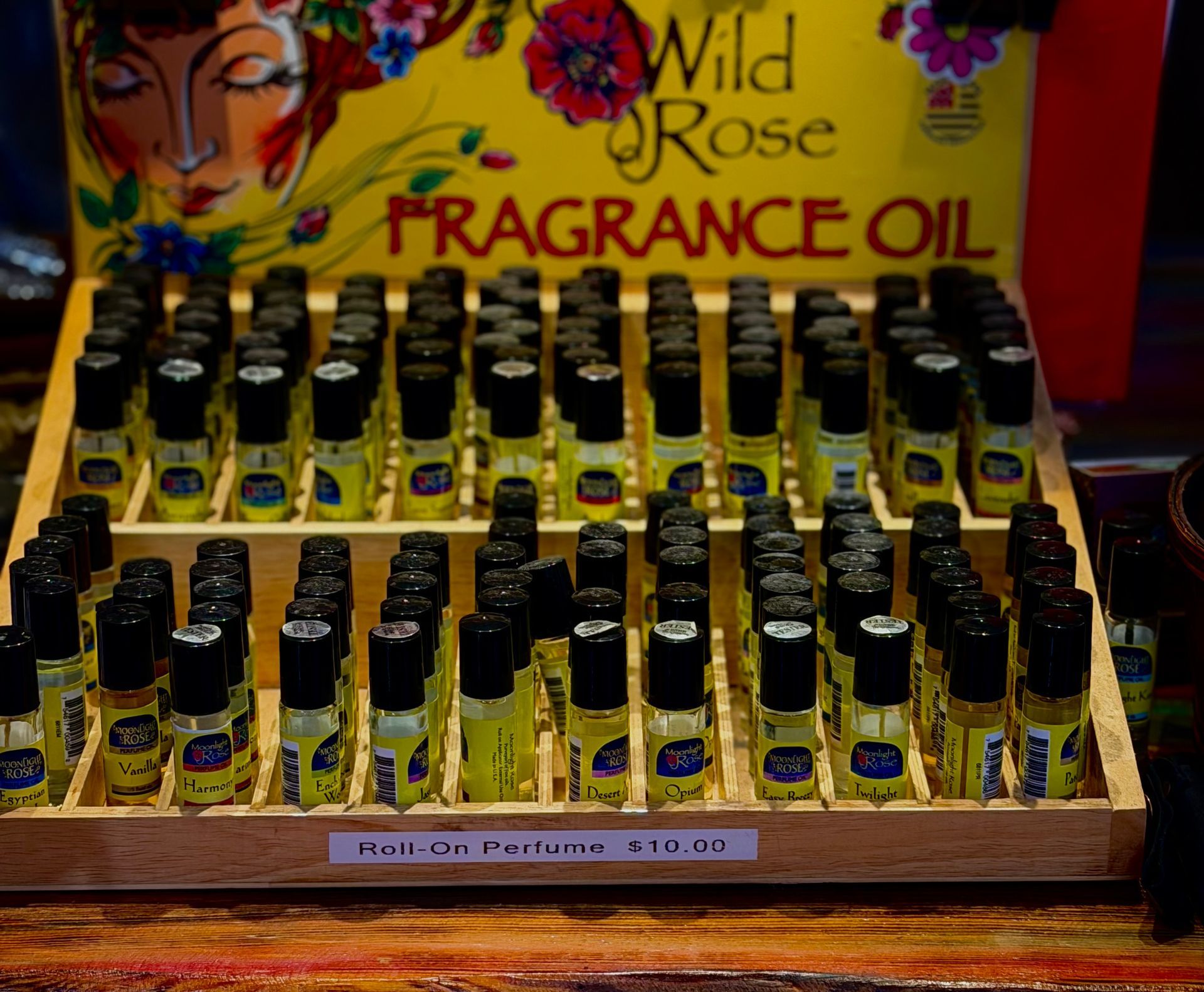 Display of small fragrance oil bottles in a wooden tray with Wild Rose packaging behind them