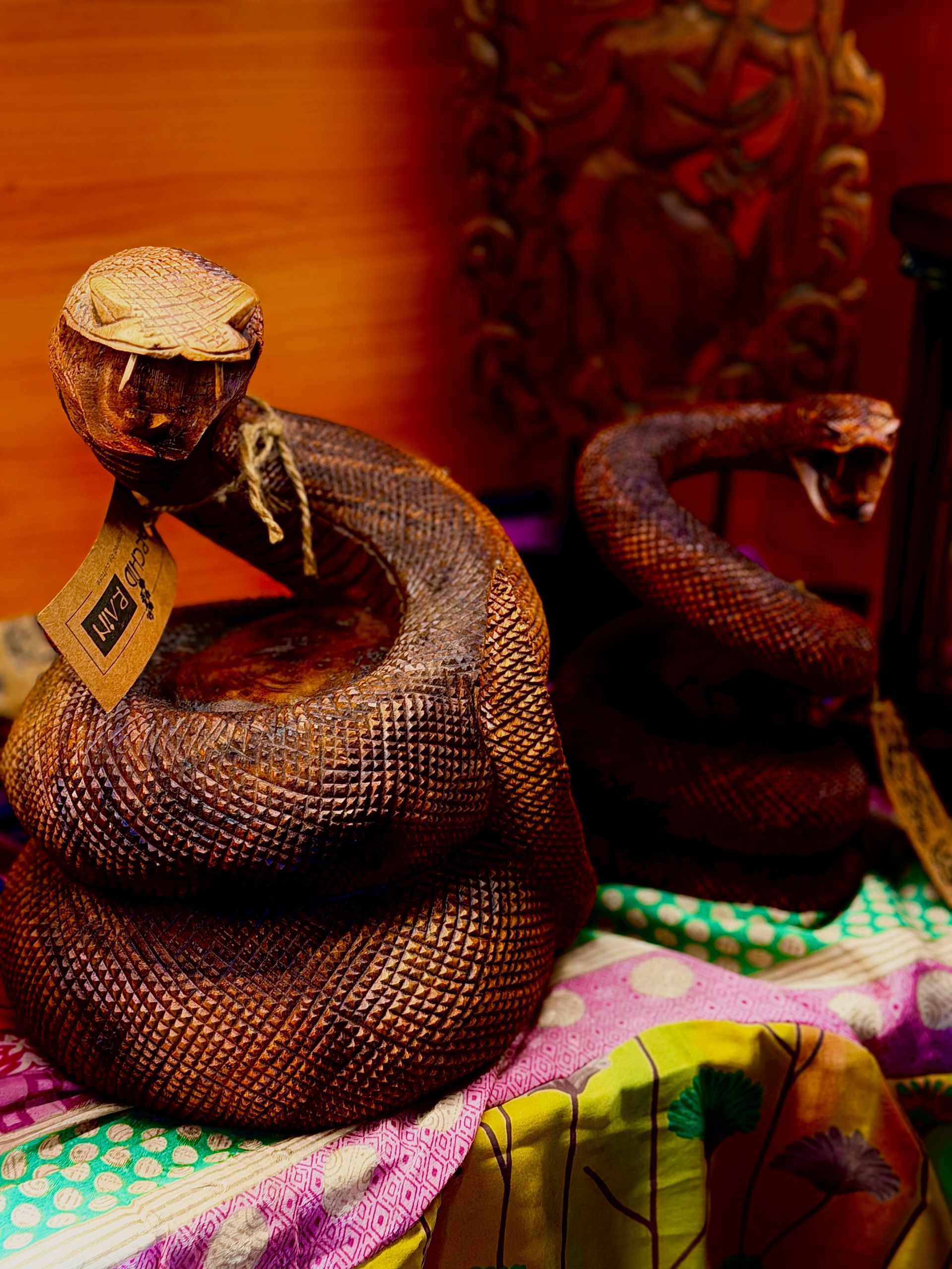 Coiled brown cobra statues on a colorful cloth against an orange wall.