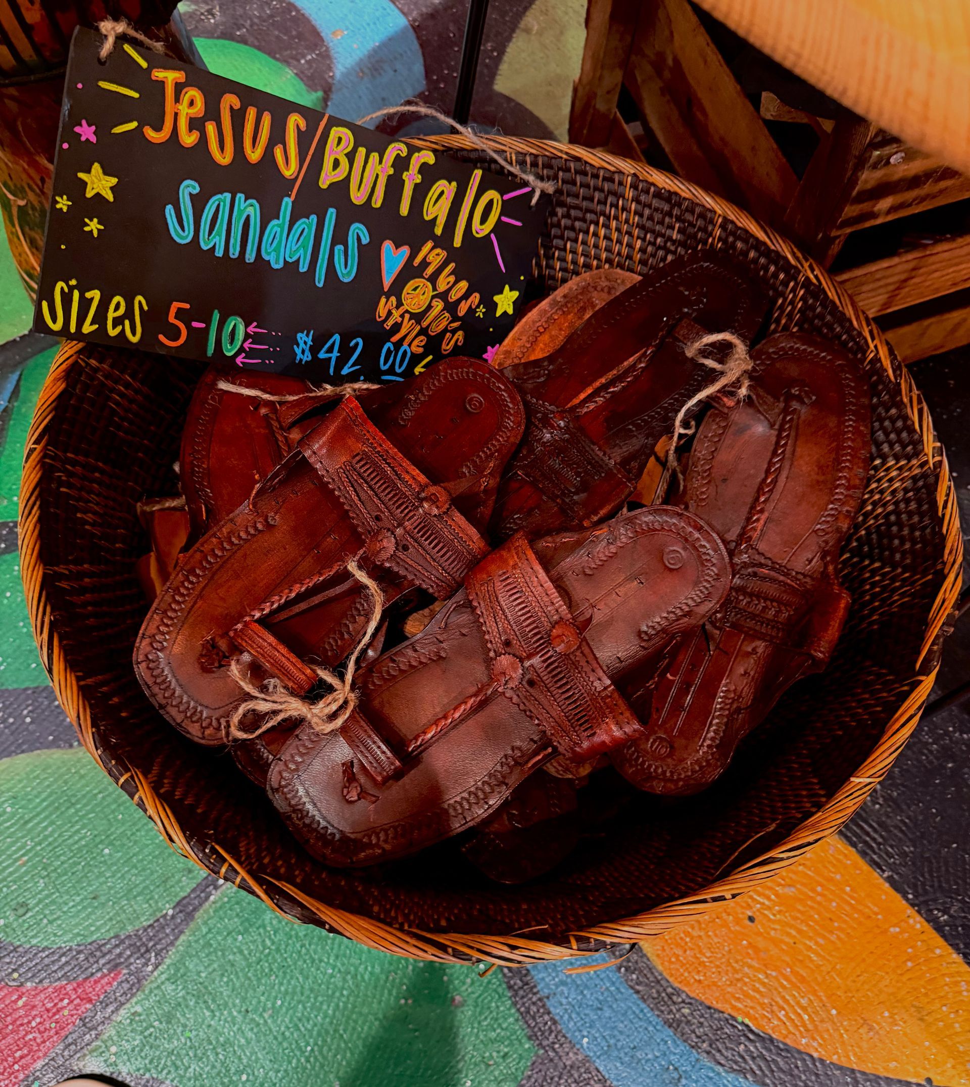 Brown woven leather sandals with a handmade sign showing sizes and price.