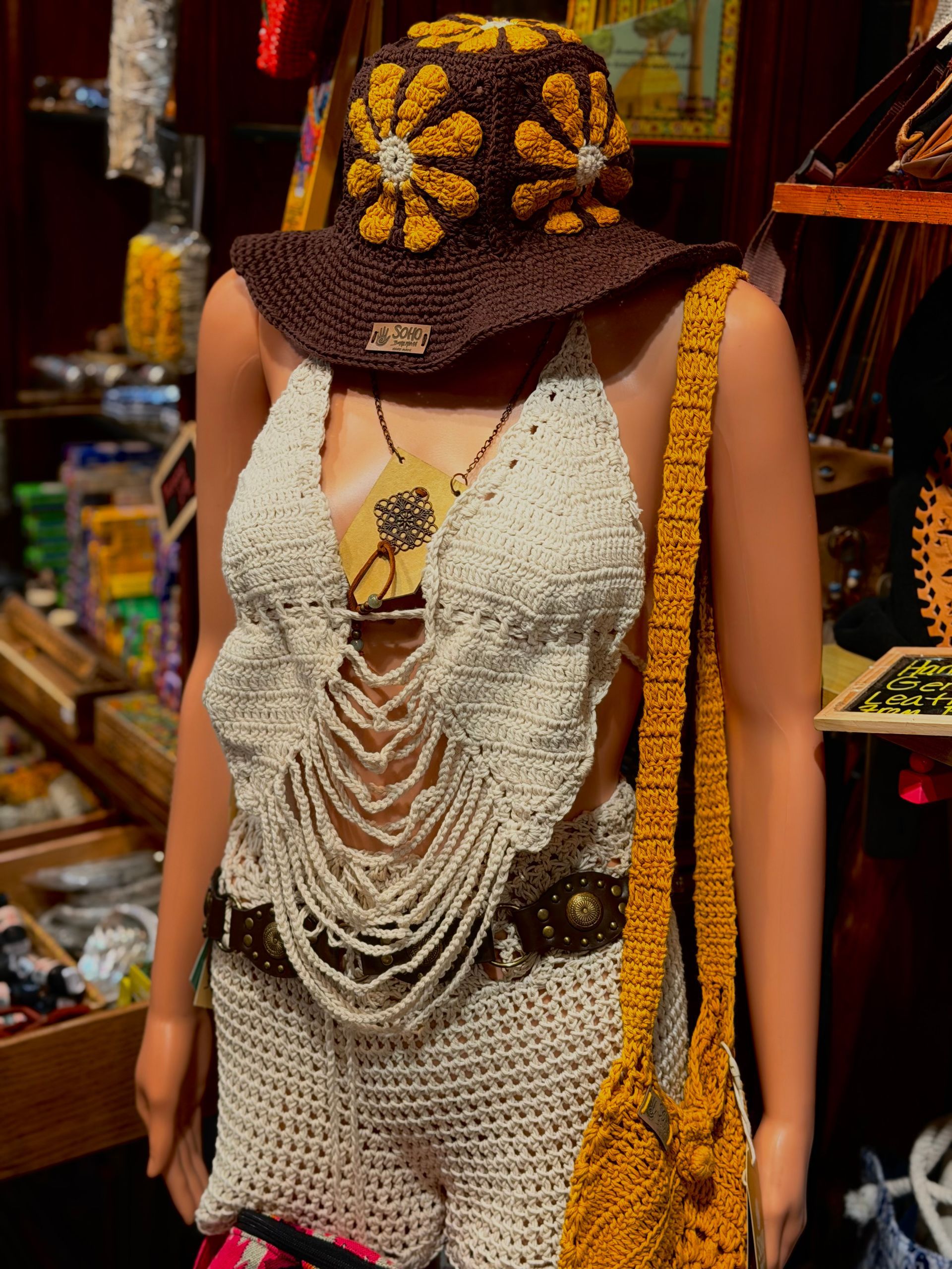 Mannequin wearing a crocheted white top and brown floral hat with a yellow woven bag in a shop