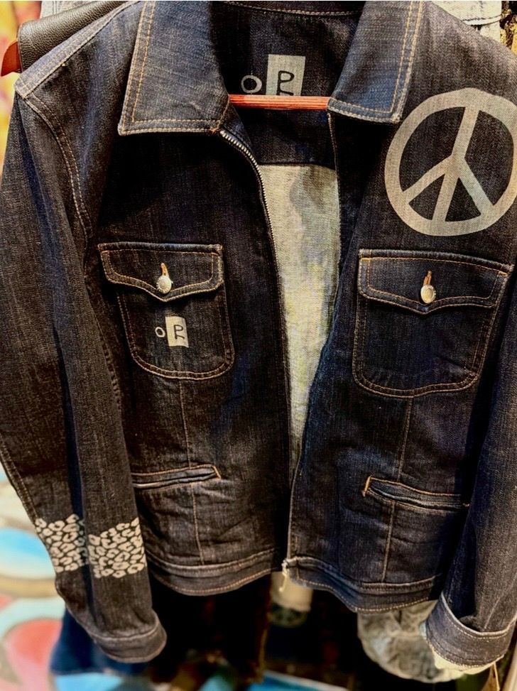 Denim jacket with peace sign patch and patterned cuffs on a display hanger.