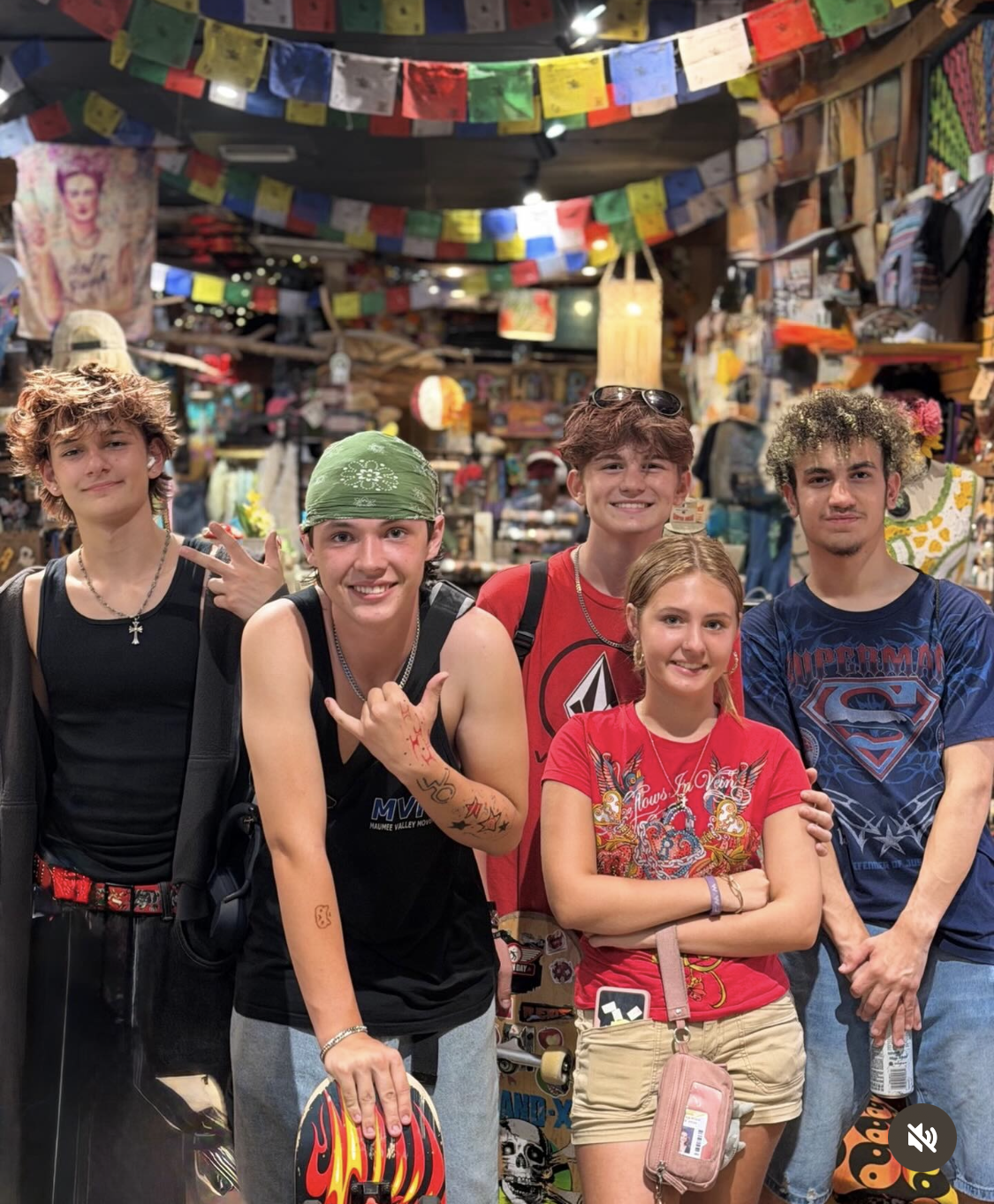 Five people posing in a colorful shop, with prayer flags and hanging decorations overhead.