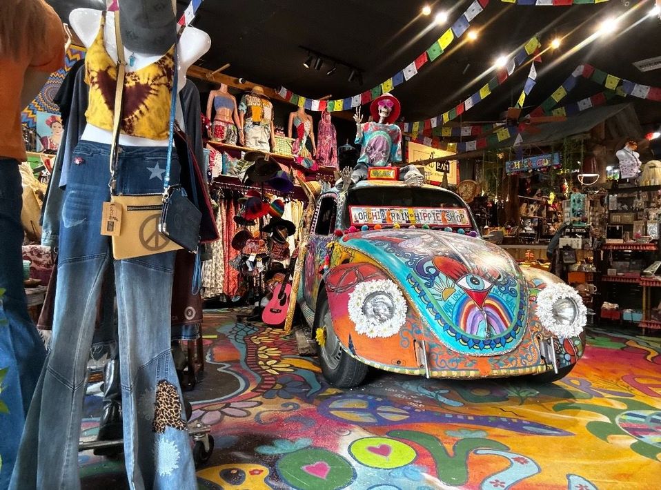 Colorful clothing display in a boutique with floral tops, patterned garments, and painted decor.