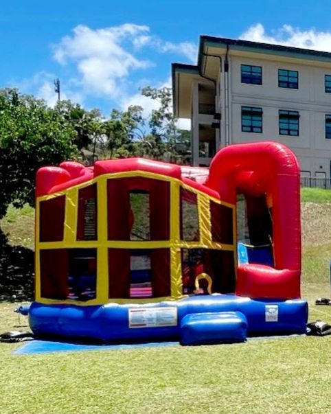 A red and yellow bouncy house is sitting in the grass in front of a building.
