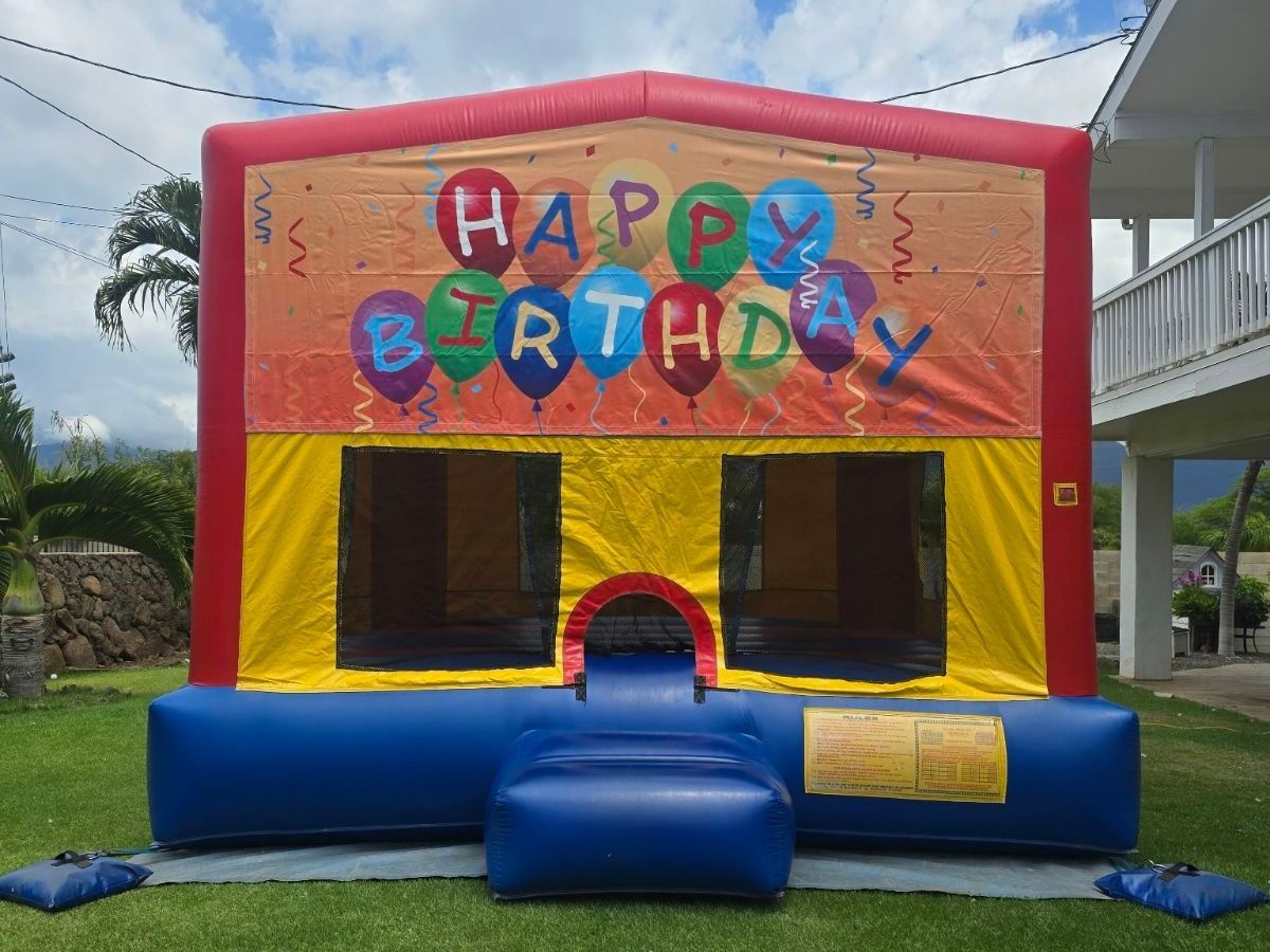 A happy birthday bouncy house is sitting on top of a lush green field.