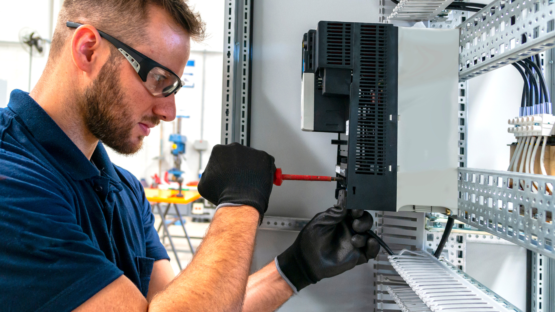 Person using a tool to inspect electrical wiring in a circuit breaker panel, with blue, yellow, and green wires.