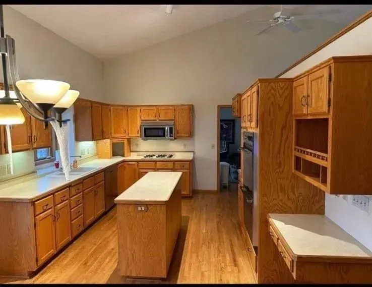 Kitchen with oak cabinets, island, and appliances. Light-colored countertops and wood floors.