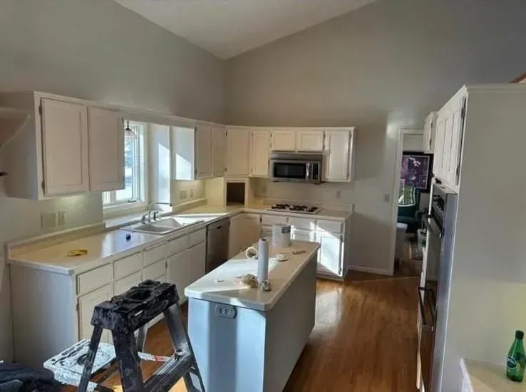 White kitchen with cabinets, island, and countertops; ladder in the foreground.
