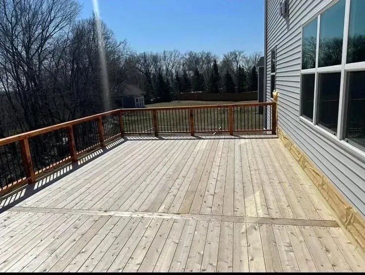 Wooden deck with railing next to a house with large windows, sunny day.
