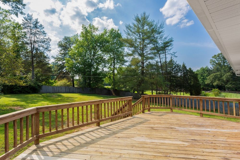 Wooden deck overlooking a grassy yard with trees, under a blue sky.