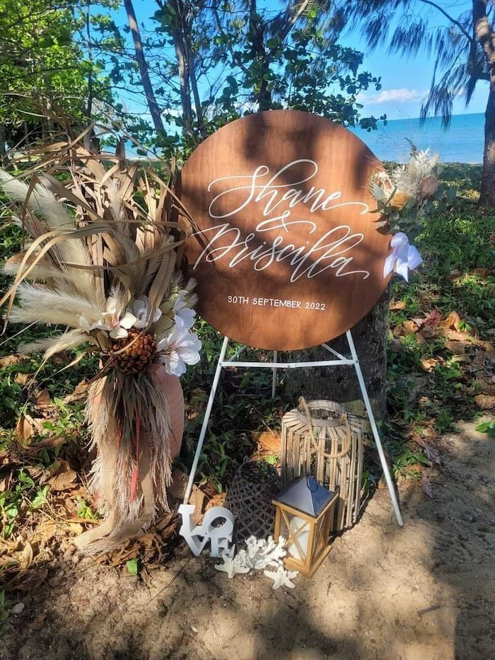 Wedding Sign: Brown Wooden Circle With White Script, Surrounded by Beach Decor — Creative Events Innisfail in Mission Beach, QLD