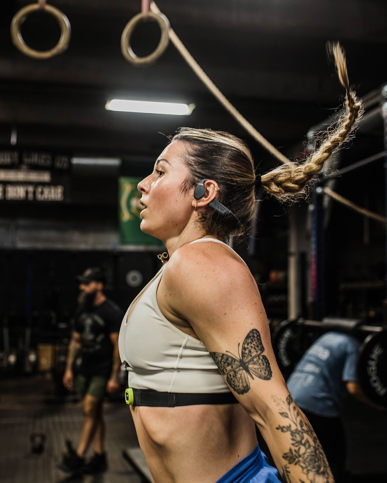 Mujer haciendo ejercicio en un gimnasio, en pleno salto con una cuerda, con un sujetador deportivo blanco y tatuajes visibles.