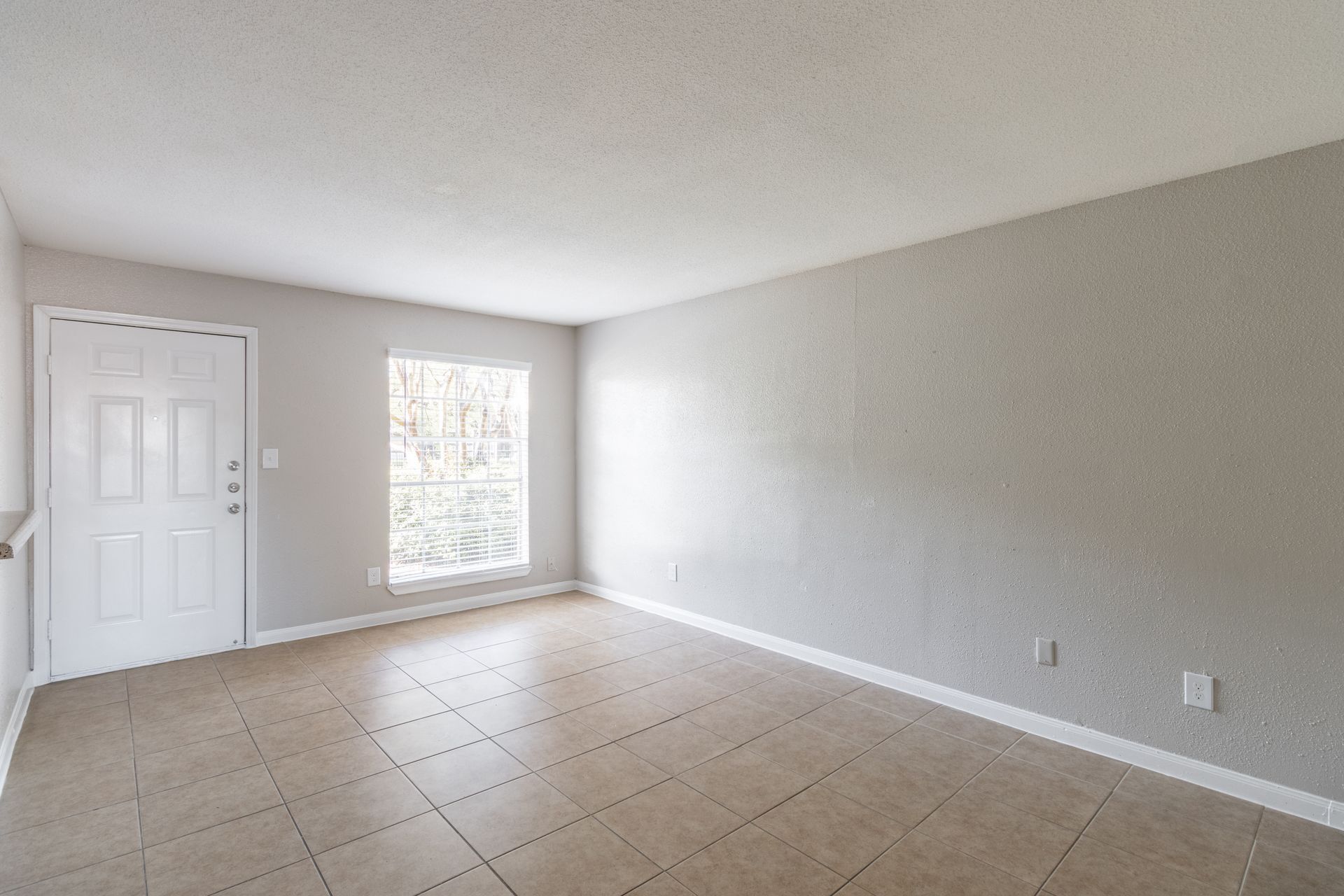 An empty living room with a window and a door.