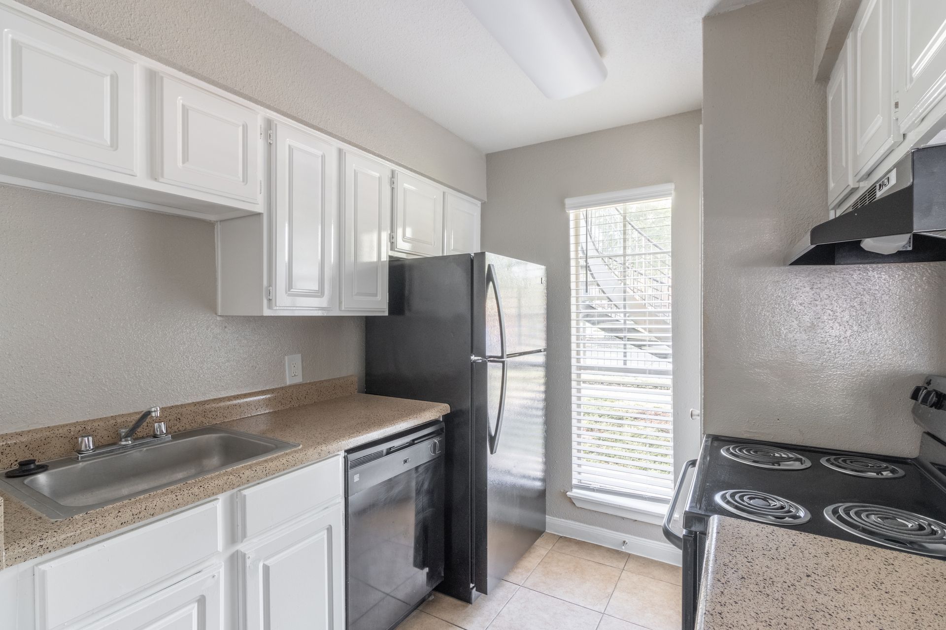 A kitchen with white cabinets , stainless steel appliances , a sink , stove and refrigerator.