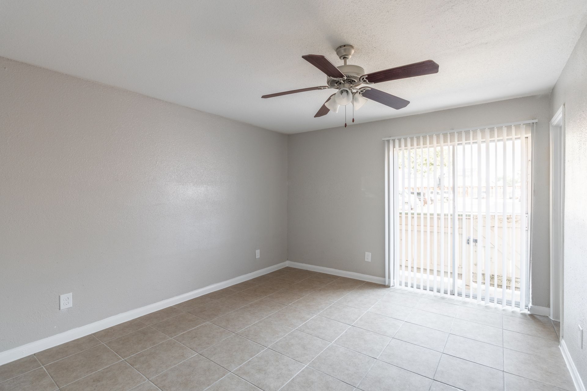 An empty living room with a ceiling fan and sliding glass doors.