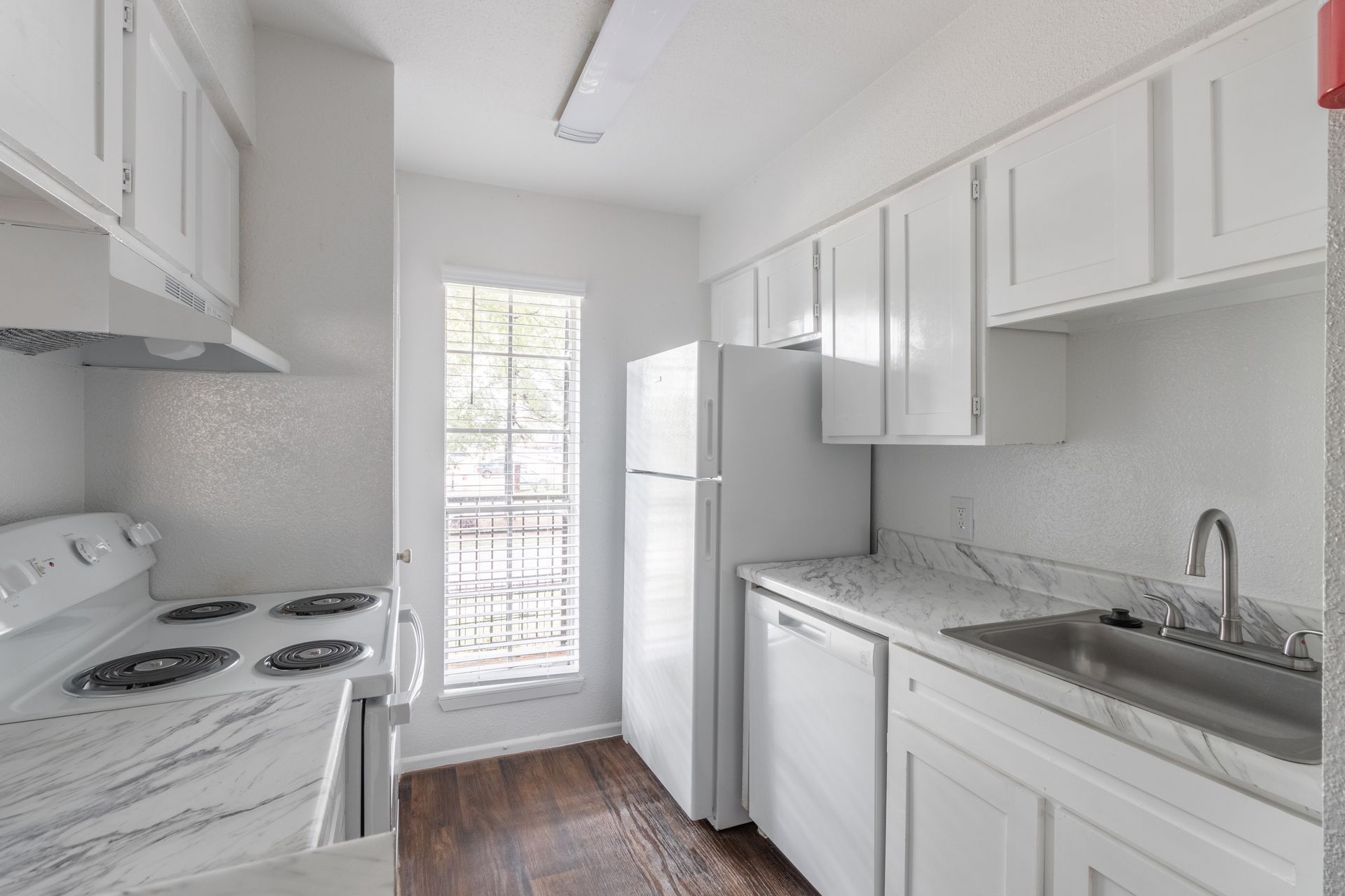 A kitchen with white cabinets , a stove , a refrigerator , and a sink.