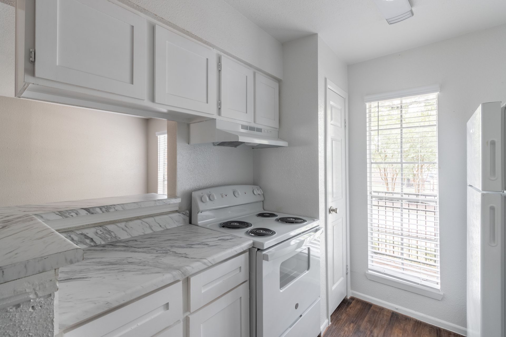 A kitchen with white cabinets , a stove , a refrigerator , and a window.