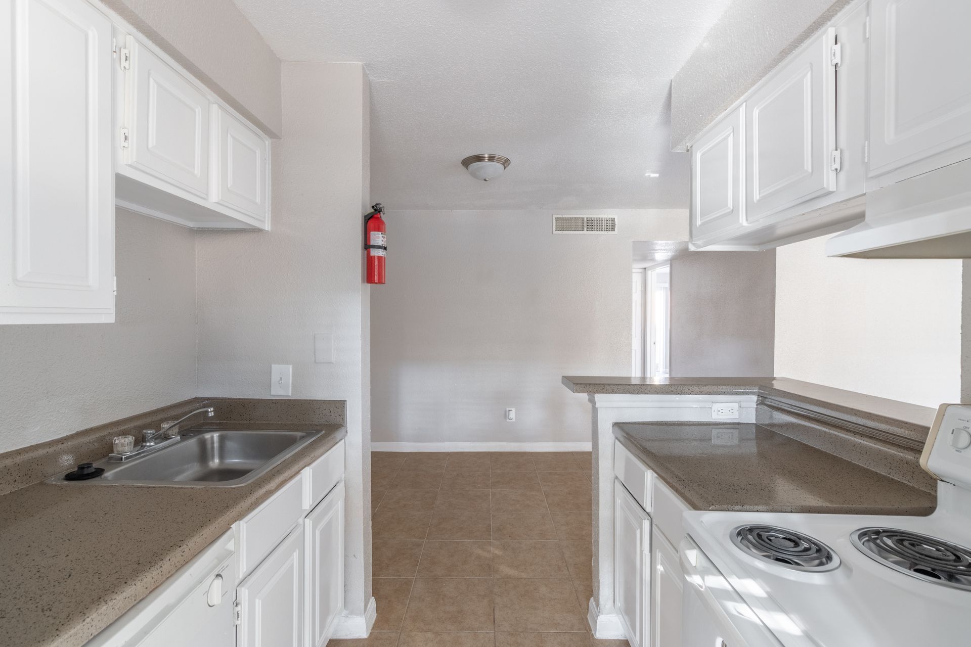 A kitchen with white cabinets , a stove , a sink and a fire extinguisher.
