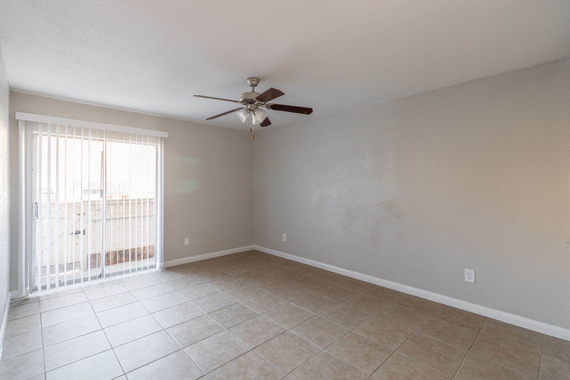 An empty living room with a ceiling fan and sliding glass doors.