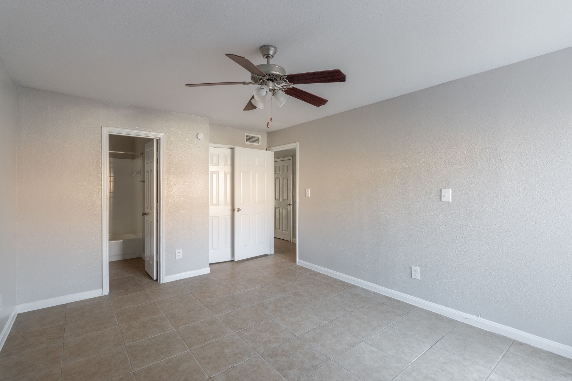 An empty bedroom with a ceiling fan and a bathroom.