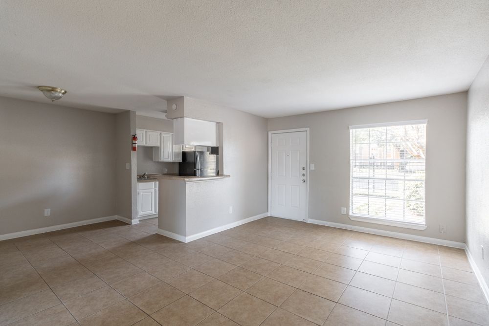 An empty living room with a kitchen in the background.