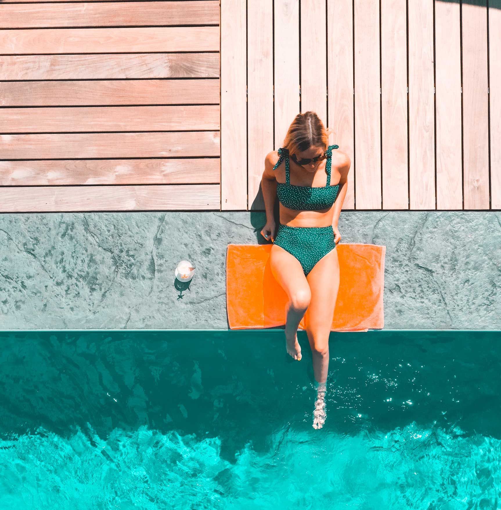 a woman in a bikini is sitting on the edge of a swimming pool .