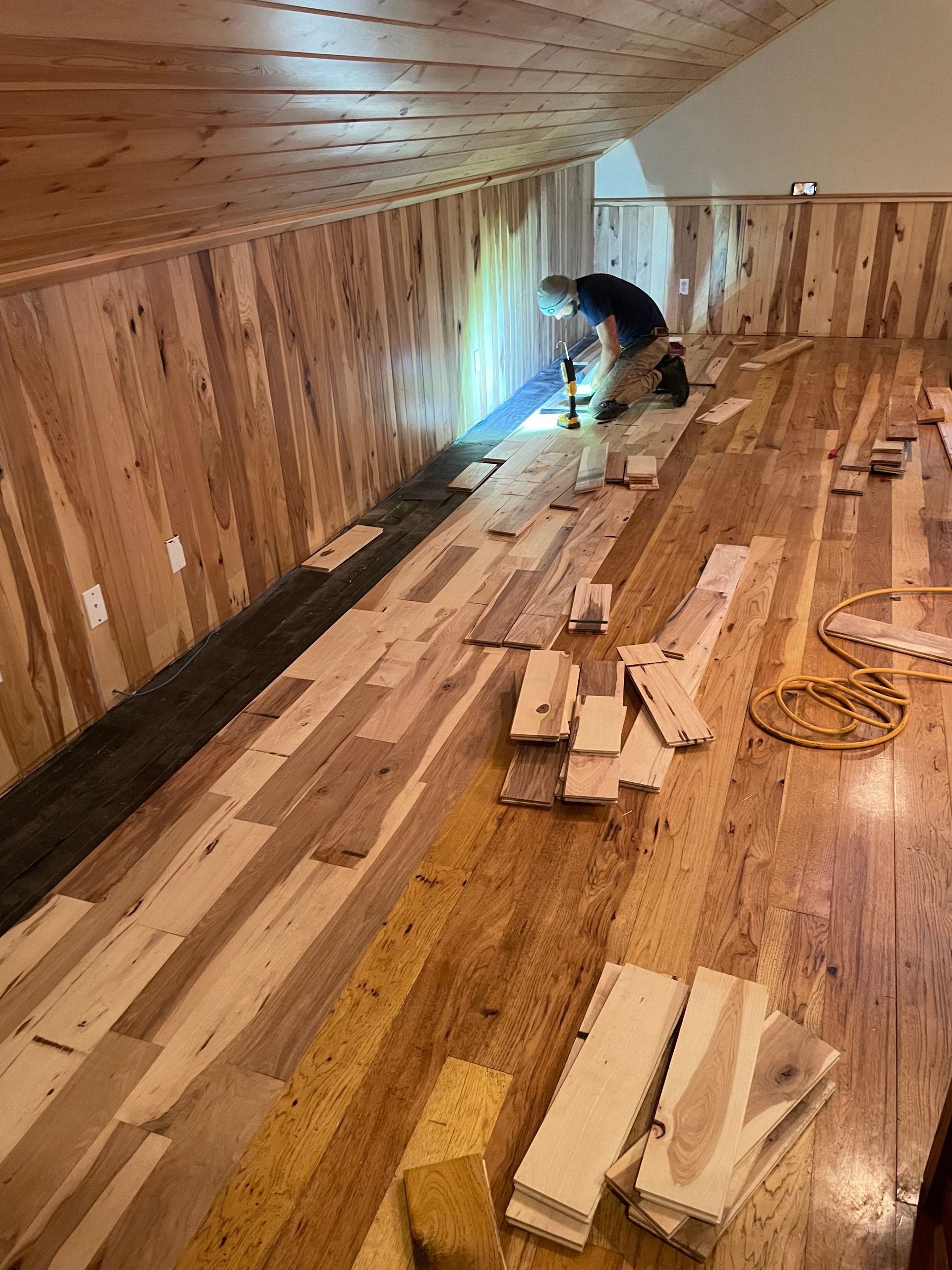 A man is working on a wooden floor in an attic.