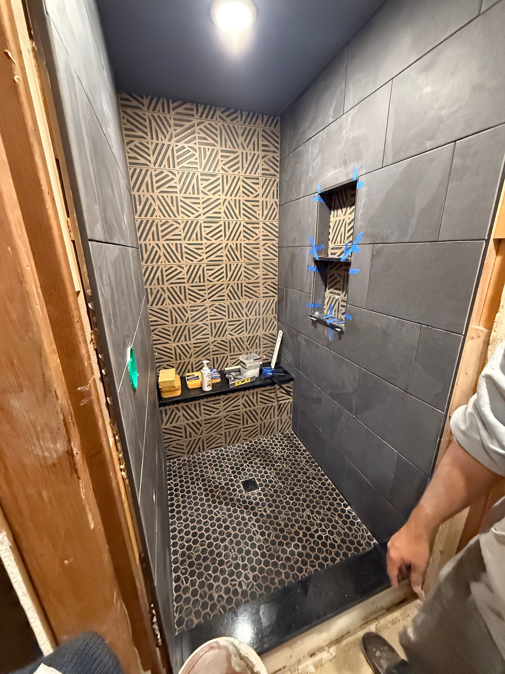 A man is standing in a bathroom with a walk in shower.