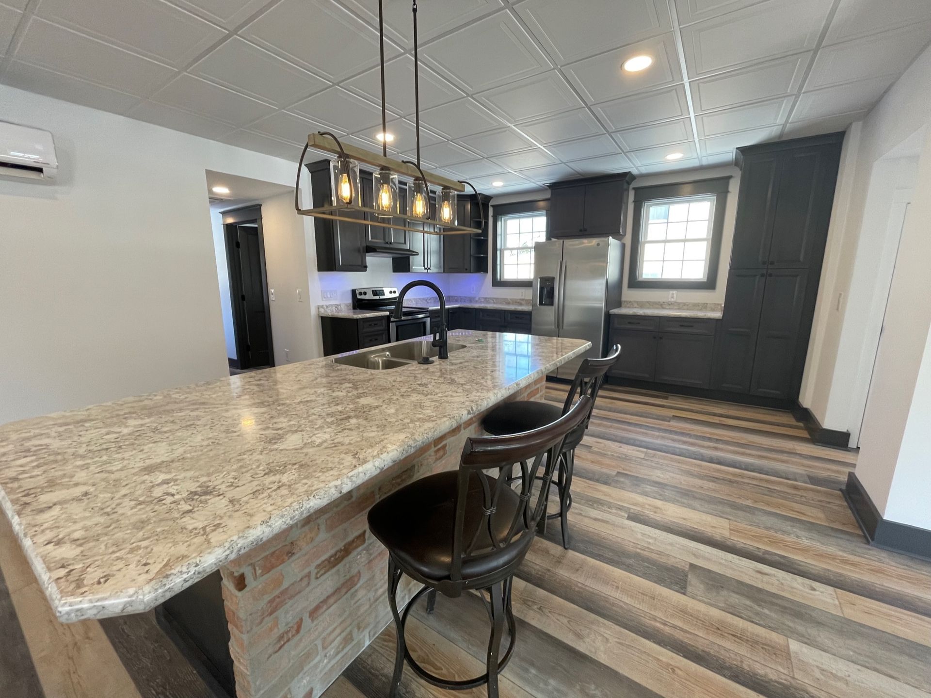 A kitchen with a large island , stools and a refrigerator.