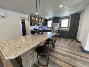 A kitchen with a large island , stools and a refrigerator.