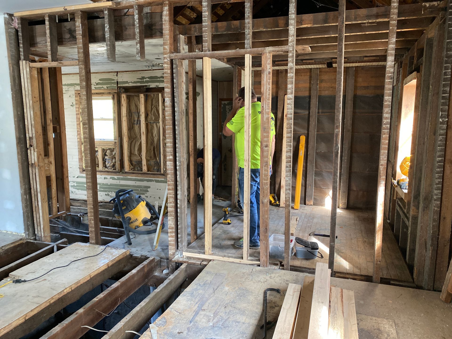 A man in a green shirt is standing in the middle of a house under construction.