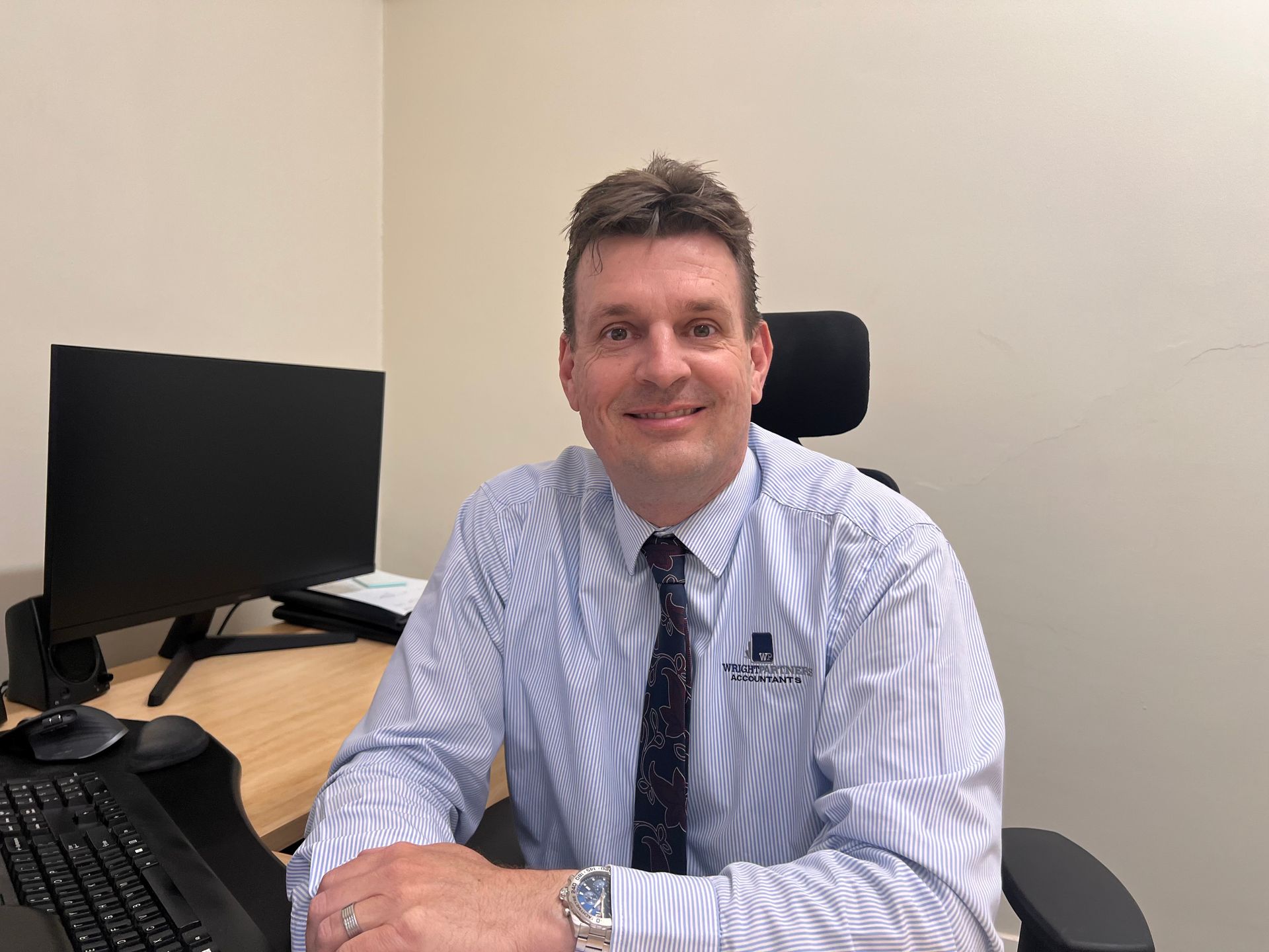 Man in striped shirt and tie smiles at desk with computer monitor — Wright Partners in Dubbo, NSW
