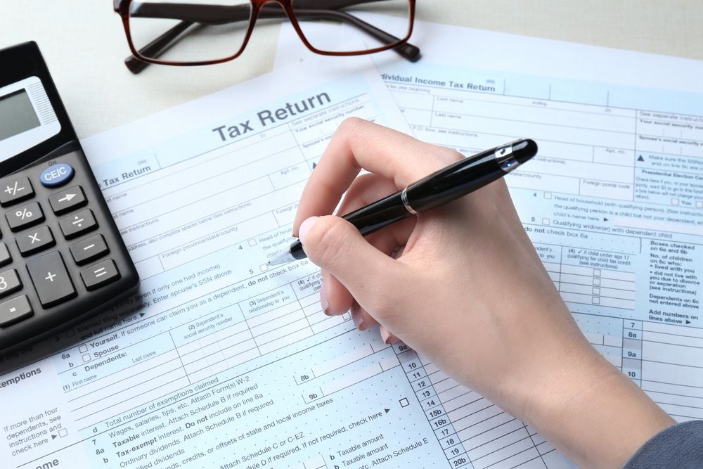 Person Filling out A Tax Return Form with A Pen, Calculator, and Glasses Nearby — Wright Partners in Walgett, NSW