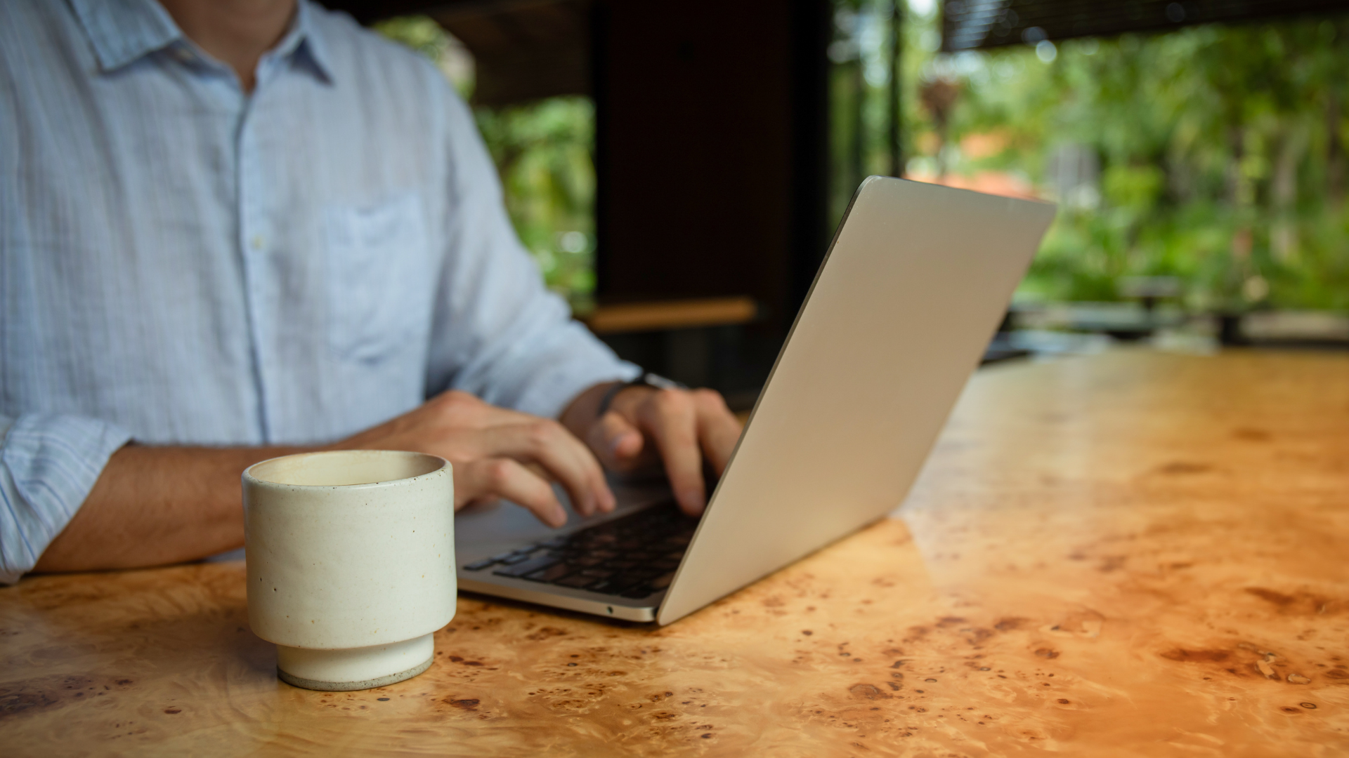 A person sitting at a desk with a laptop, watching an online video, with their hands resting on their head.