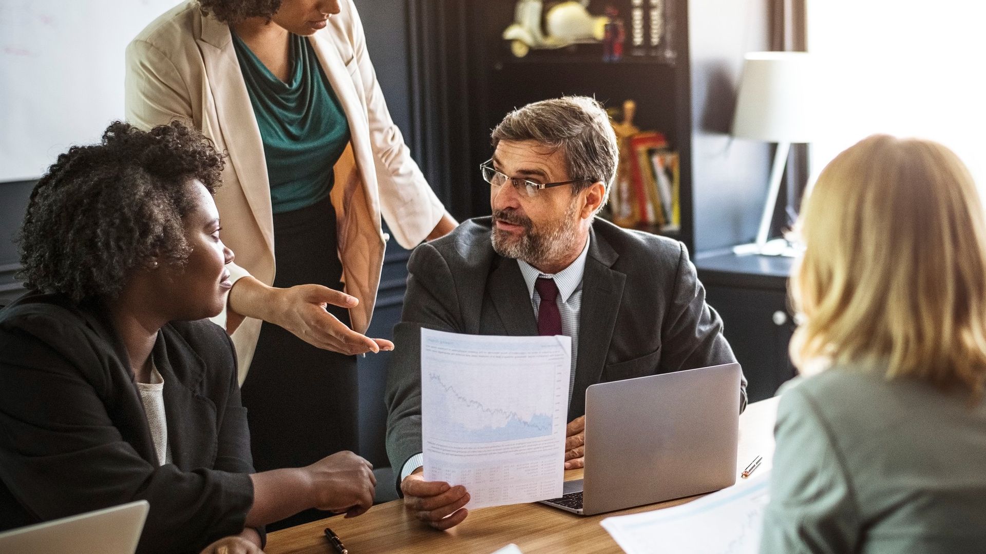 Small business meeting with four people reviewing papers around a table in a bright office.