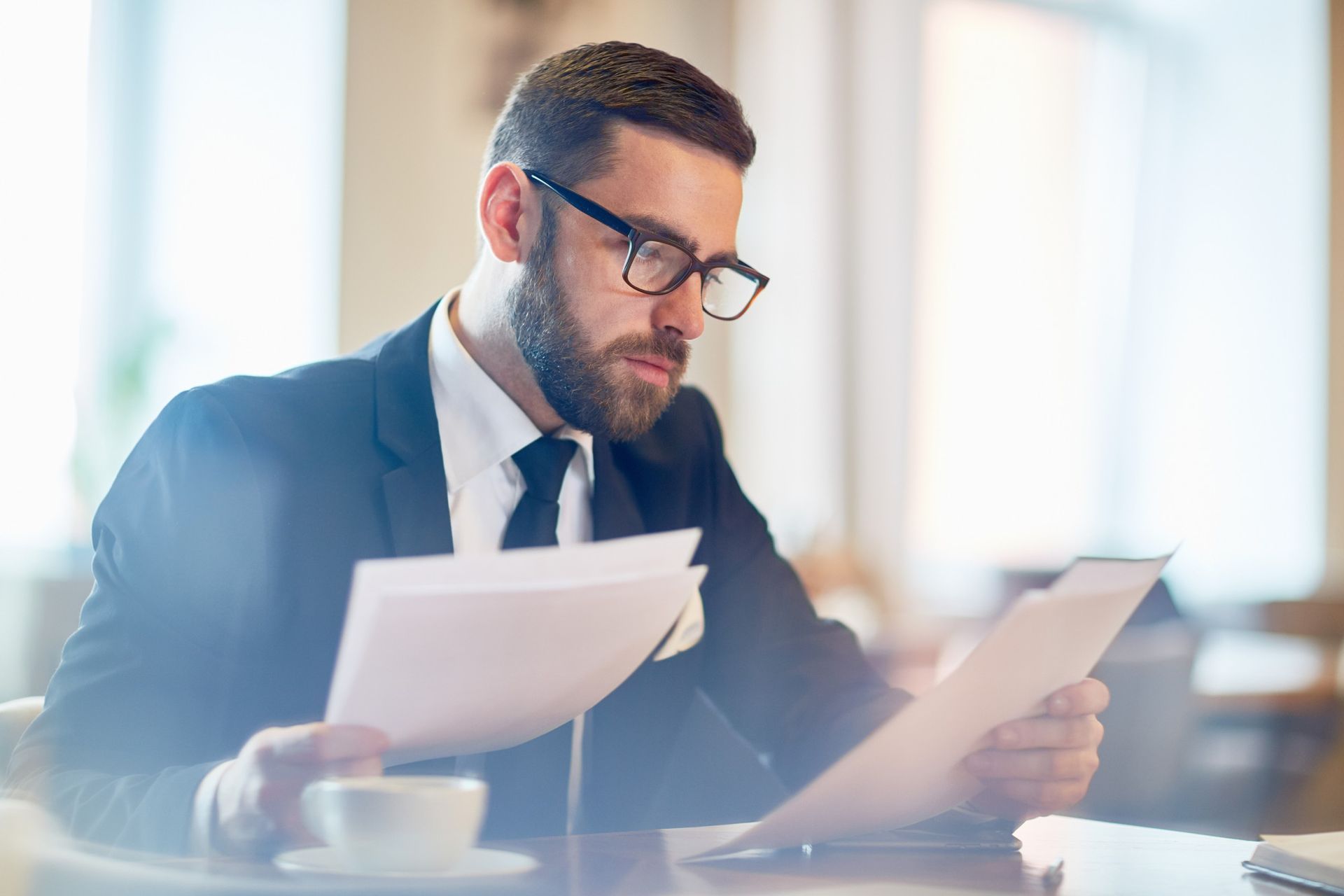 Man in a suit reviewing documents and a tablet at a bright office desk