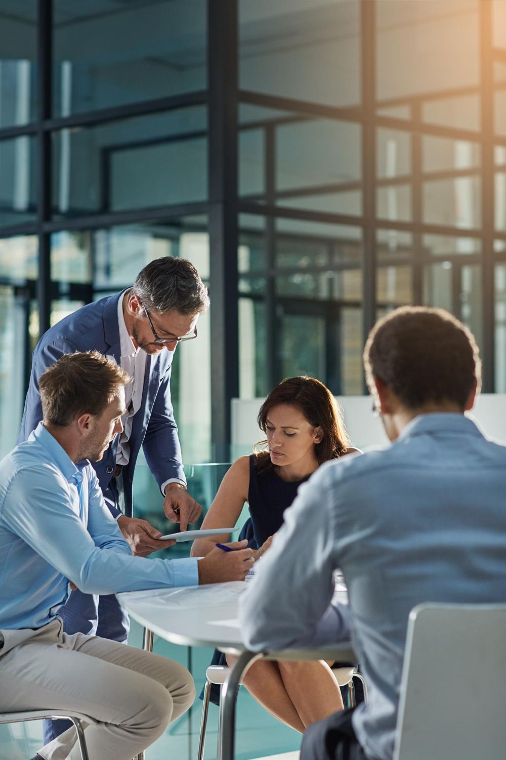 Team meeting around a table in a modern glass office, with notes and a laptop on display.