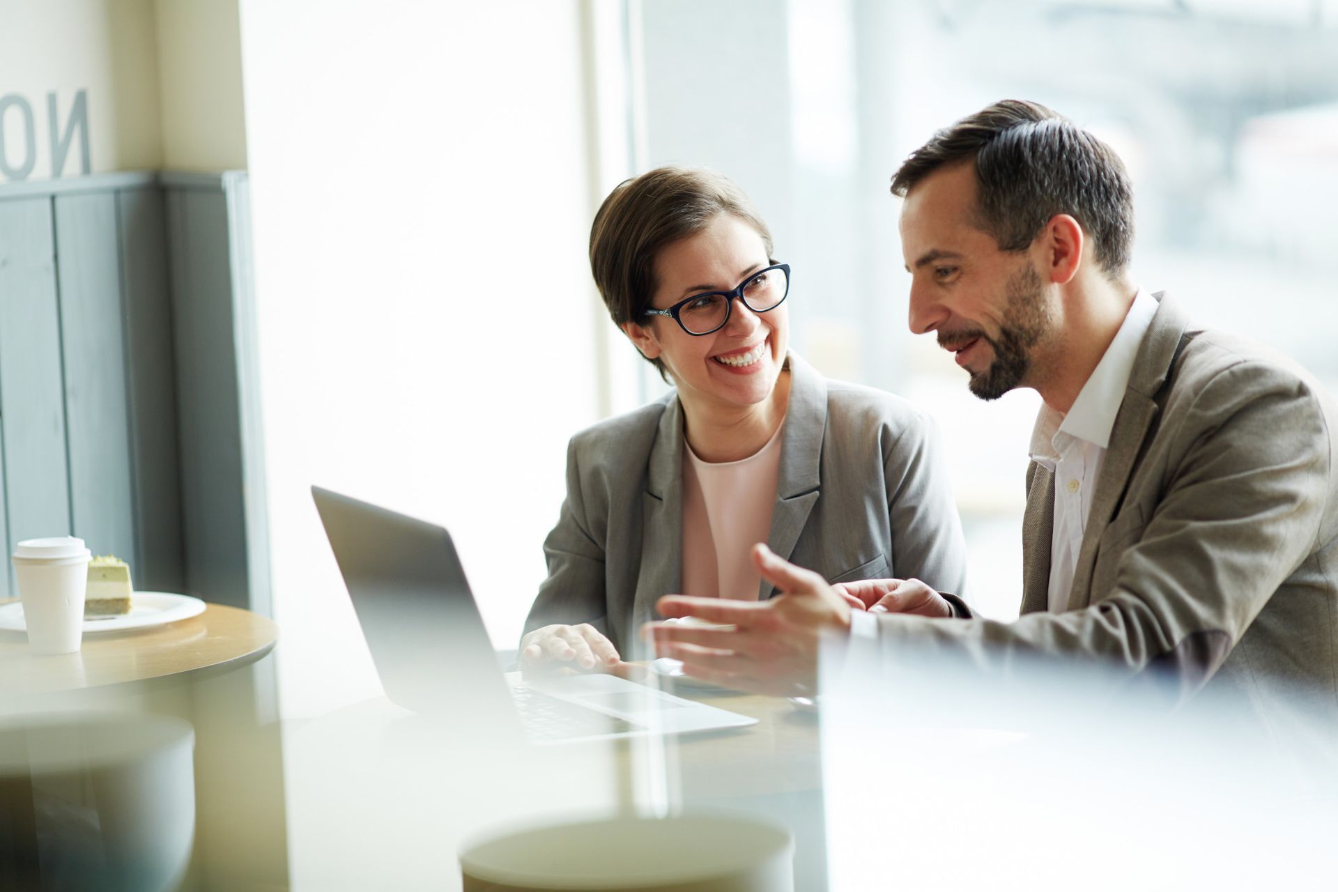 Two colleagues smiling and discussing work at a laptop in a bright office
