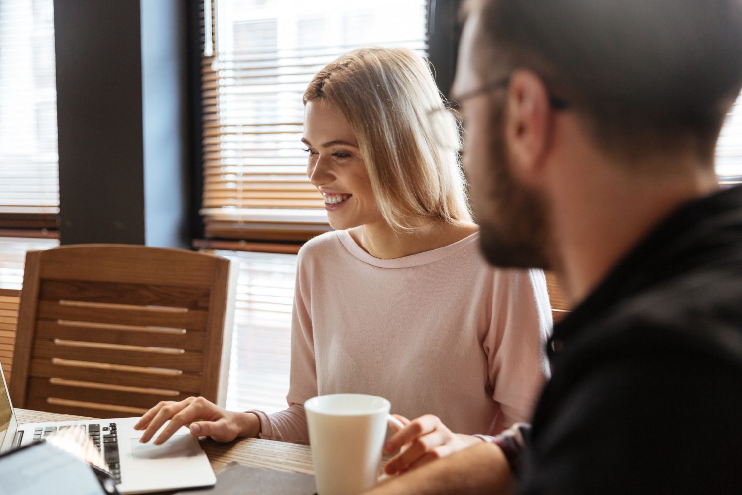 Two people talking at a table with a laptop and coffee in a bright office room