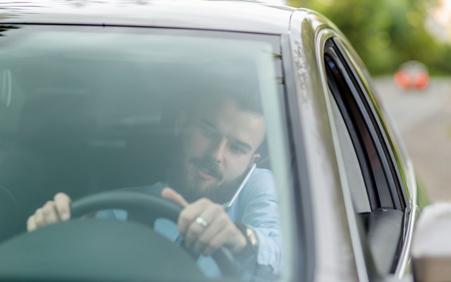 Driver seen through windshield, looking forward and gripping the steering wheel in a parked car.