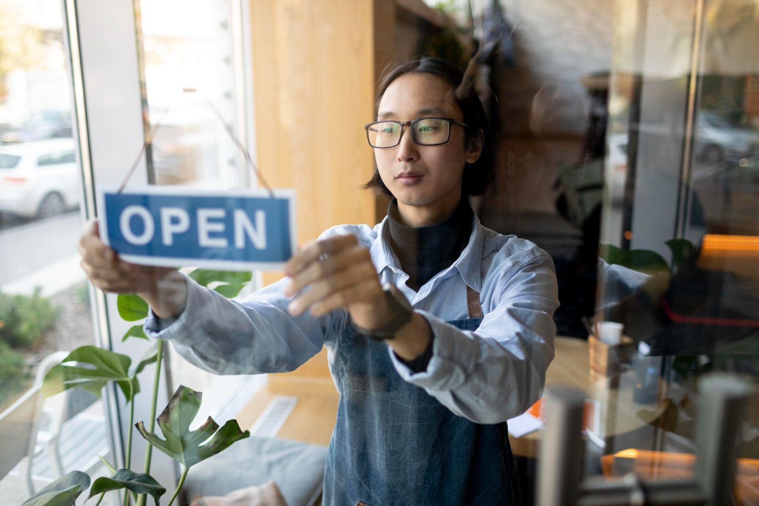 Person hanging an OPEN sign on a glass door in a bright storefront