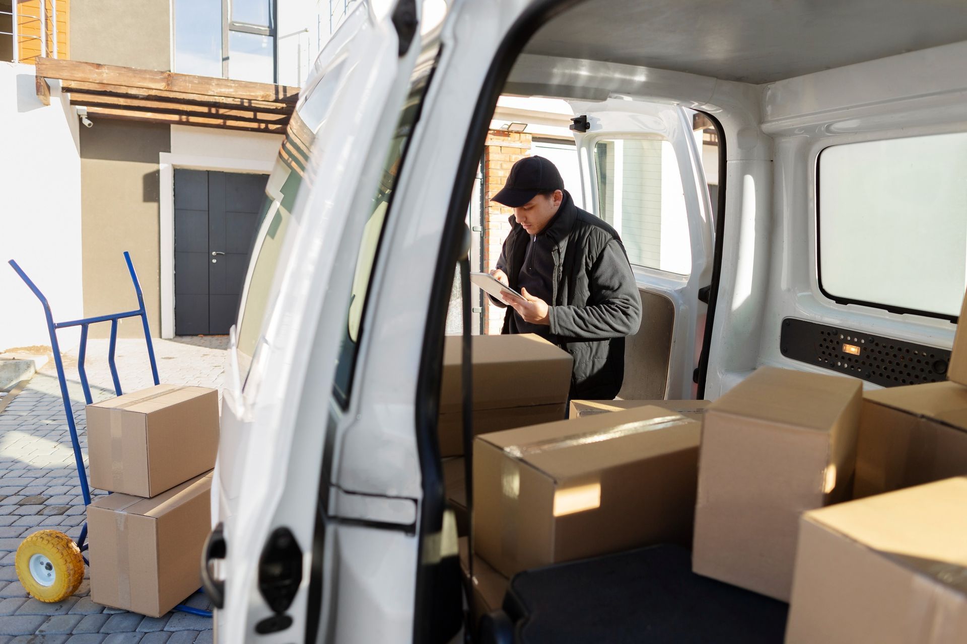 Person loading cardboard boxes into a white van in a driveway.