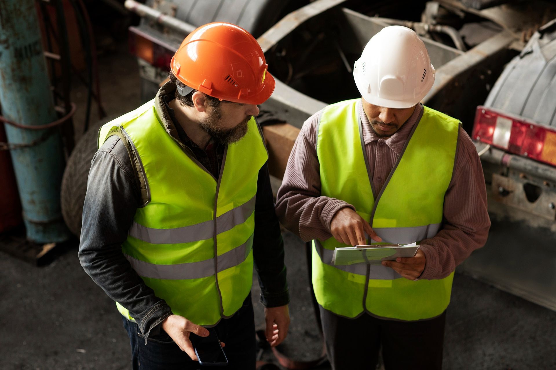 Two workers in hard hats and reflective vests reviewing a tablet at a construction site