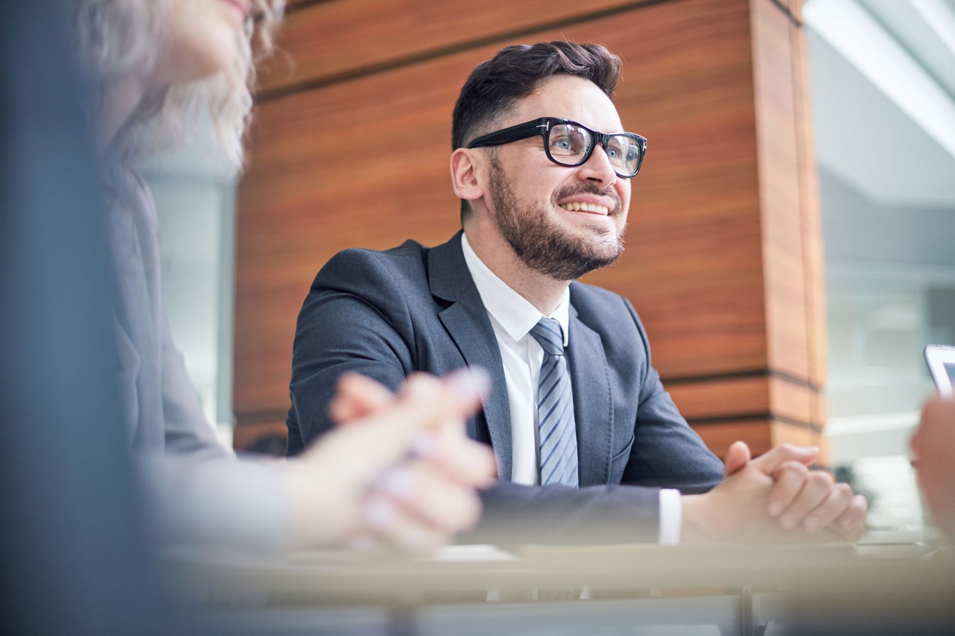 Business meeting in a modern office, with a man in a suit smiling at the table.