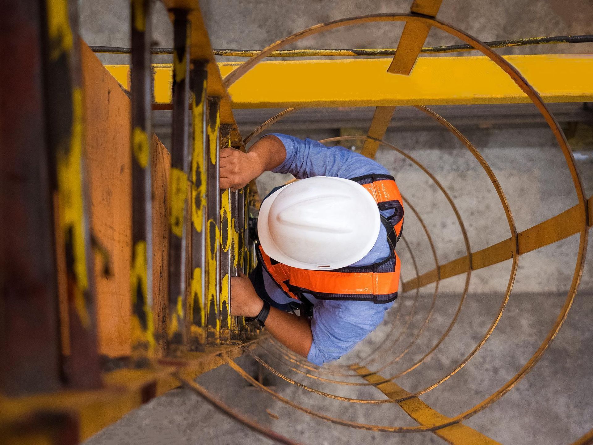 Worker in white hard hat climbing a yellow metal ladder inside a spiral structure