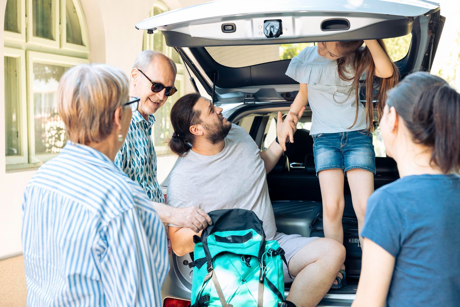 People loading bags into an SUV, with the hatch open at a home driveway.