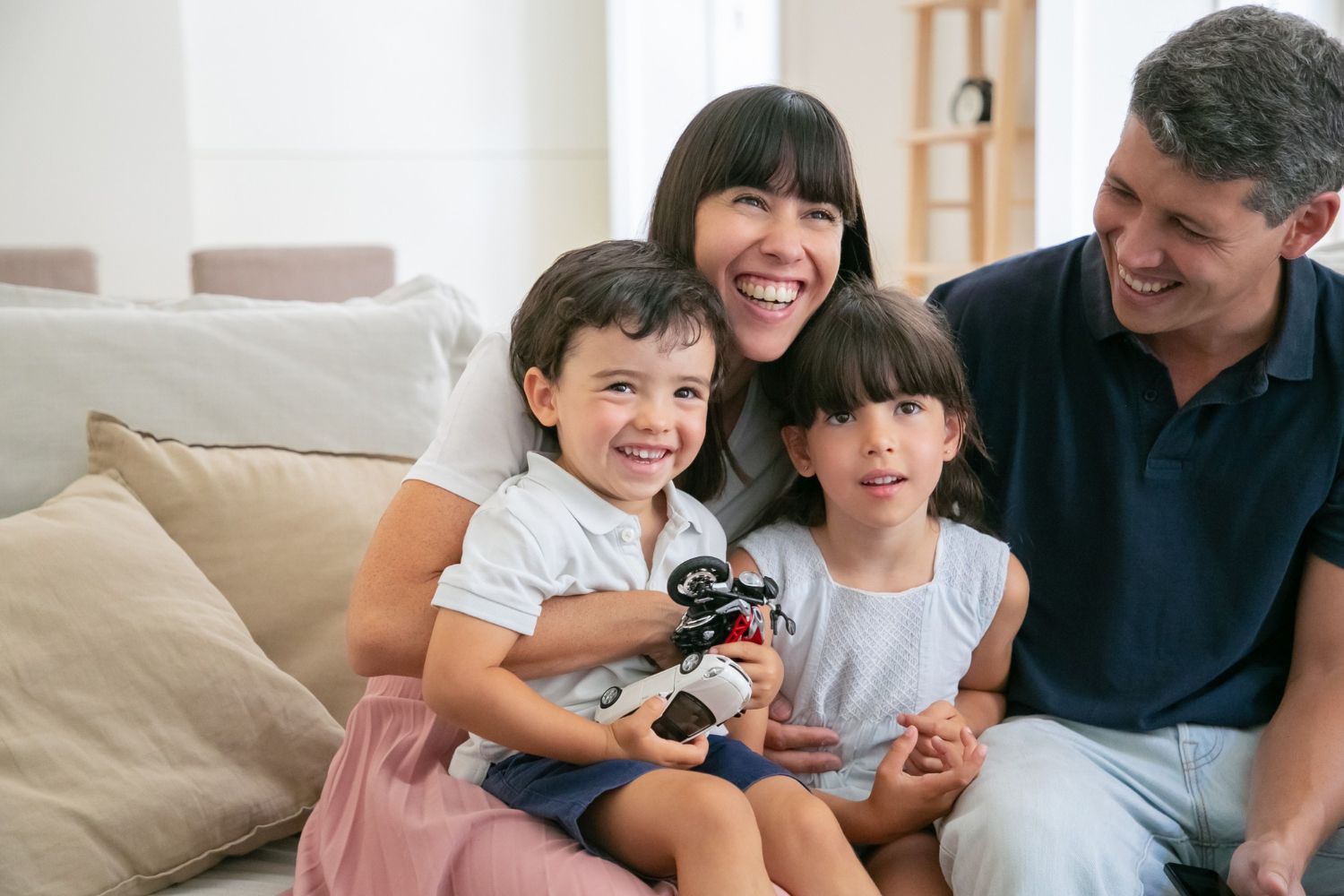 Smiling family sitting on a couch, with two children holding a toy camera.