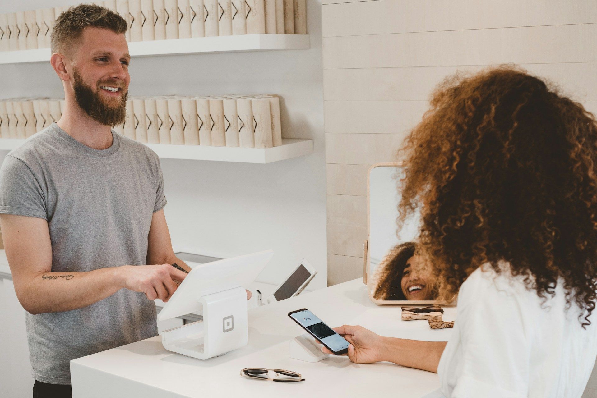 Customer paying at a counter with a card terminal while a cashier smiles nearby